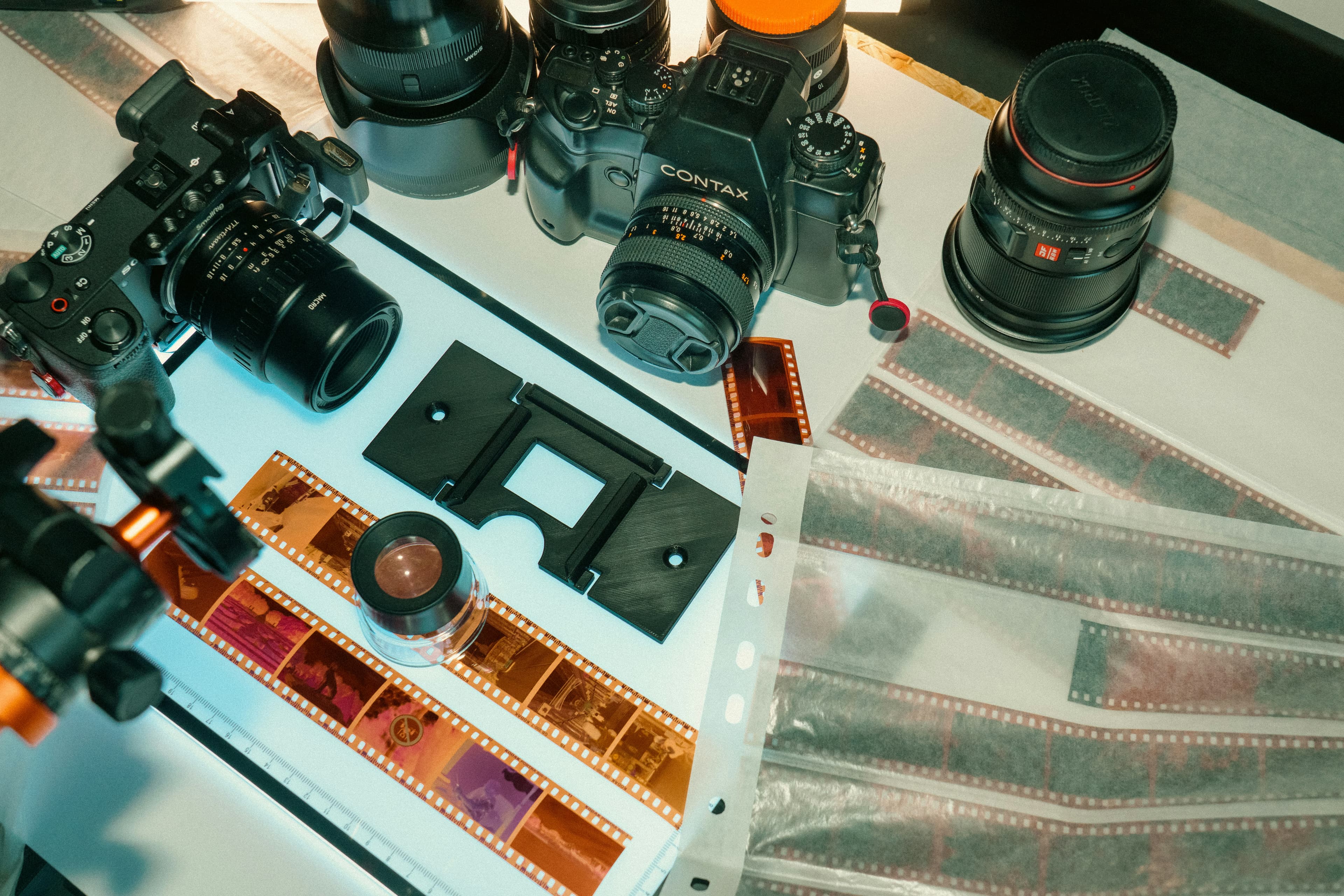 Cameras, lenses, and film negatives arranged on a light table for inspection and scanning.